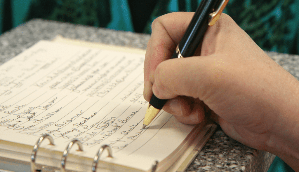 Photo by Ildar Sagdejev. Someone signing their name and their information into a book, similar to how the Book of Remembrance will contain our names and deeds.